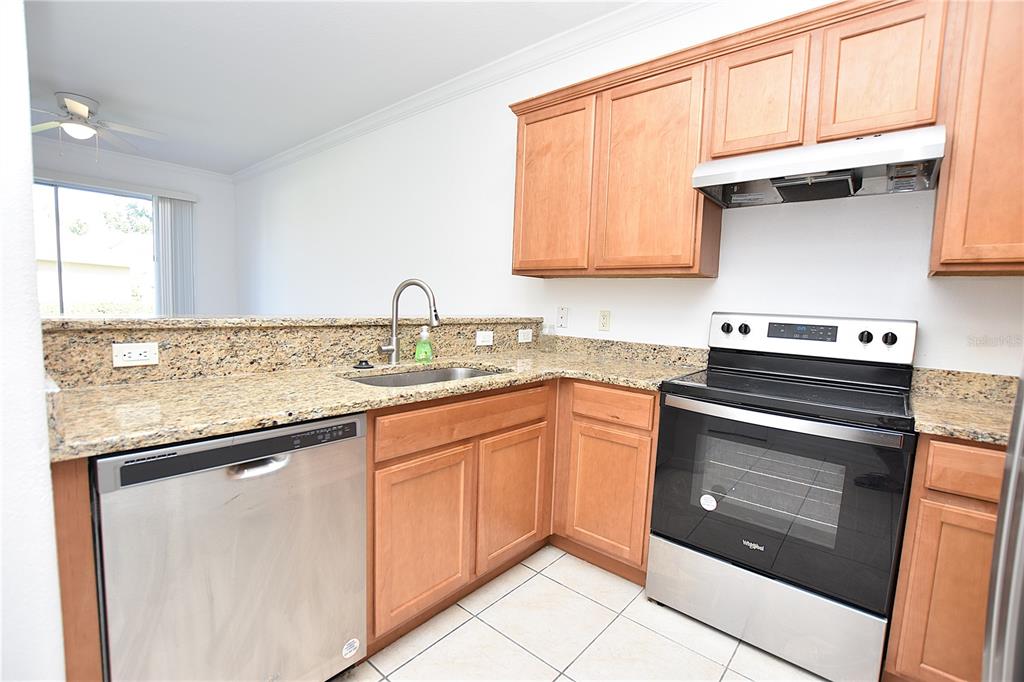 A kitchen with wood cabinets, granite countertops, stainless steel appliances, and tile flooring — 6352 SEDGEFORD DRIVE, LAKELAND, FL