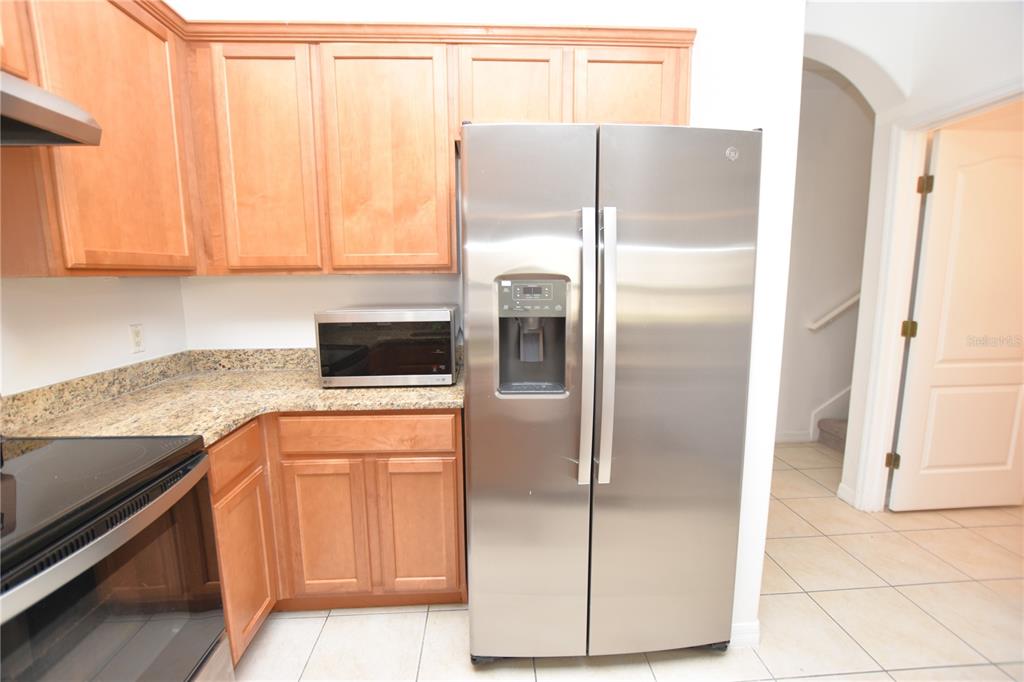 A kitchen features light wood cabinets, granite countertops, and a stainless steel refrigerator — 6352 SEDGEFORD DRIVE, LAKELAND, FL