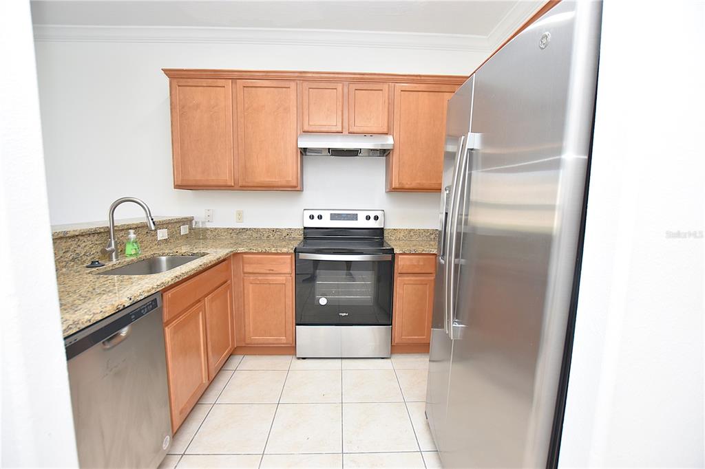 A kitchen features light wood cabinets, granite countertops, stainless steel appliances, and tile flooring — 6352 SEDGEFORD DRIVE, LAKELAND, FL