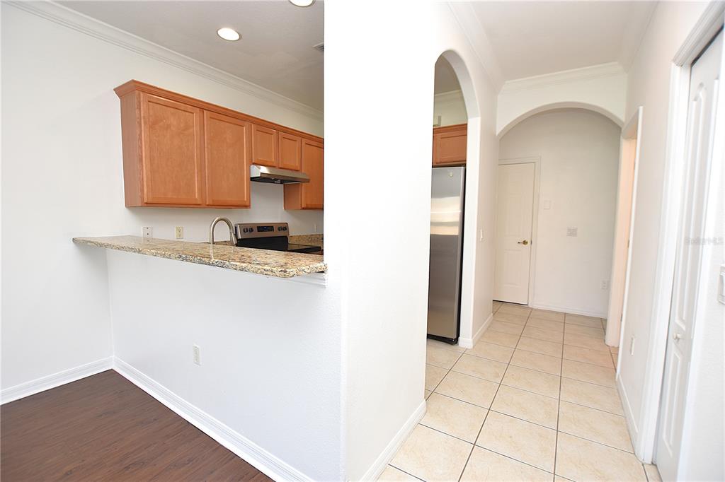 A kitchen with wood cabinets, granite countertops, and a tile floor leads into a hallway — 6352 SEDGEFORD DRIVE, LAKELAND, FL