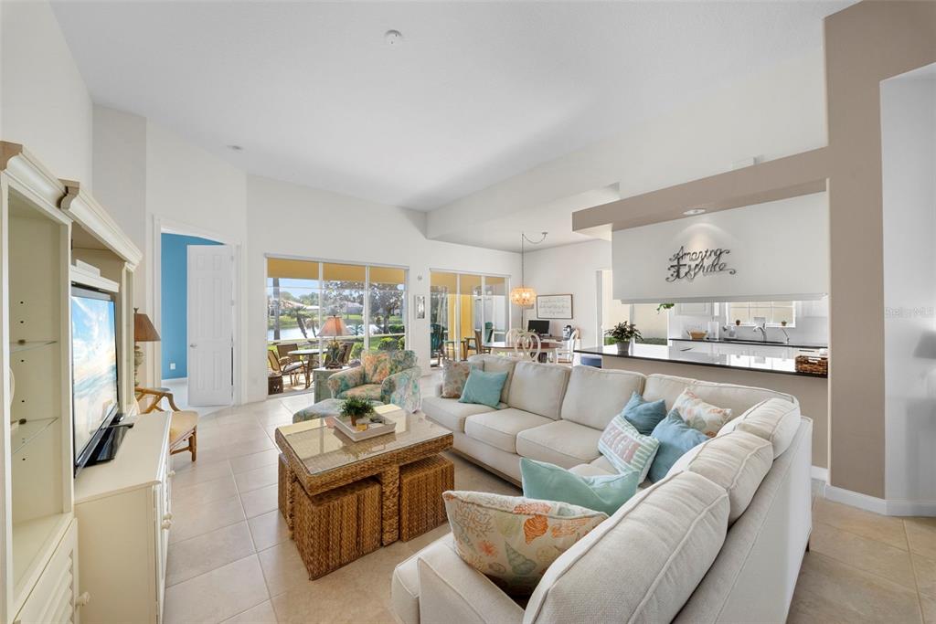 A bright living room features a large sectional sofa, a coffee table, and sliding glass doors — 7687 ULIVA WAY, SARASOTA, FL