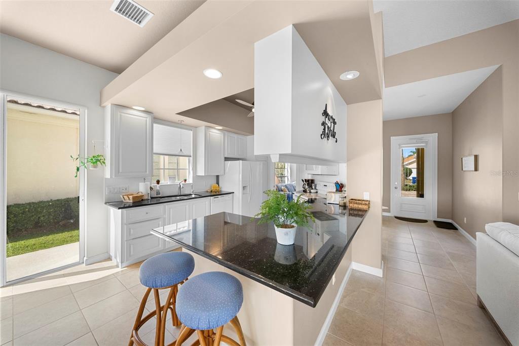 A kitchen with white cabinets, black countertops, a breakfast bar, and tile flooring — 7687 ULIVA WAY, SARASOTA, FL