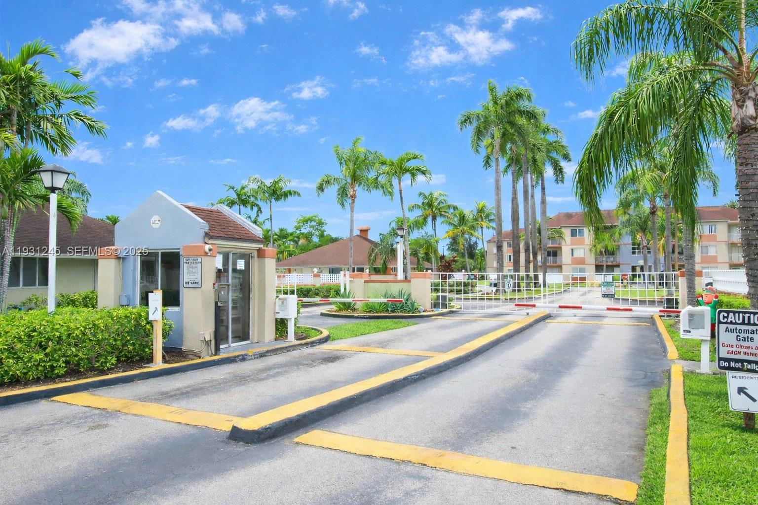 A gated entrance with a guardhouse, palm trees, and an automatic security gate — 18810 NW 57th Ave # 102, Hialeah FL 33015, HIALEAH, FL
