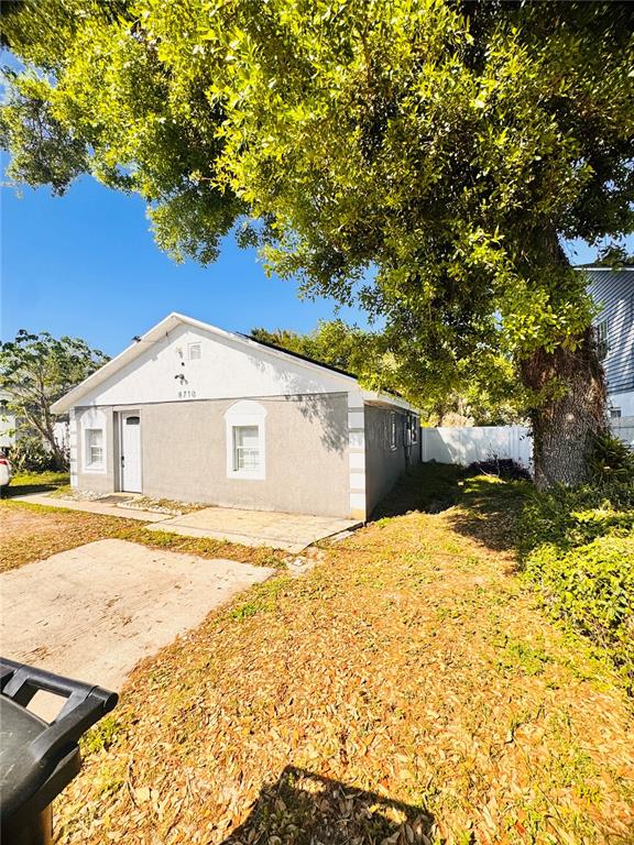 A single-story house with a light-colored stucco exterior stands beside a large tree — 8710 N TANGERINE PLACE, TAMPA, FL