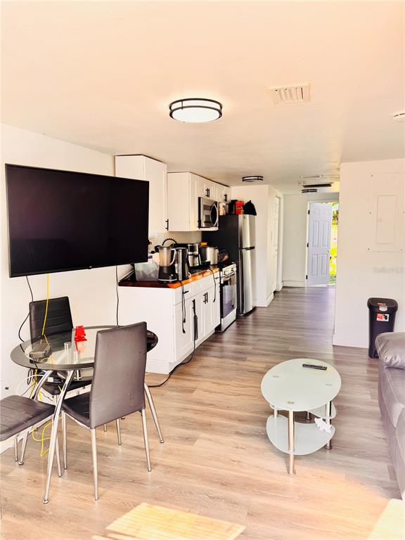 An open-concept kitchen and living area features white cabinetry, stainless steel appliances, and wood flooring — 8710 N TANGERINE PLACE, TAMPA, FL