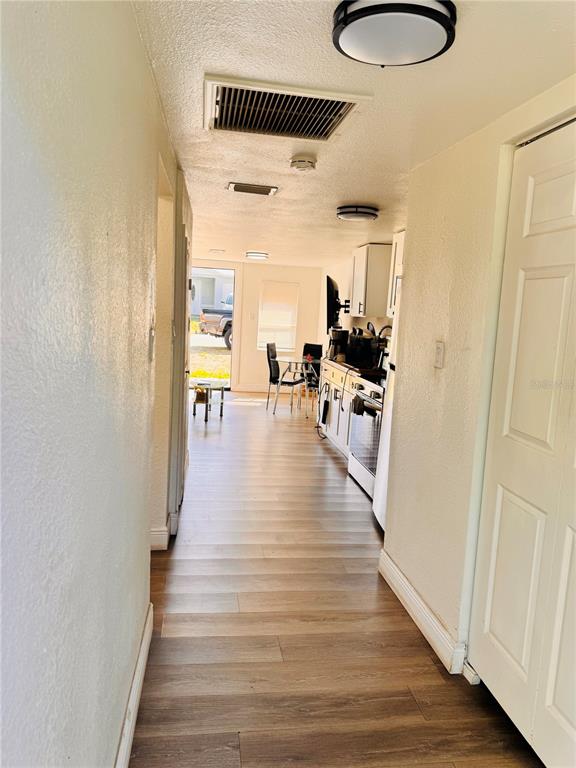 A hallway with wood-look flooring leads to a kitchen and an exterior door — 8710 N TANGERINE PLACE, TAMPA, FL