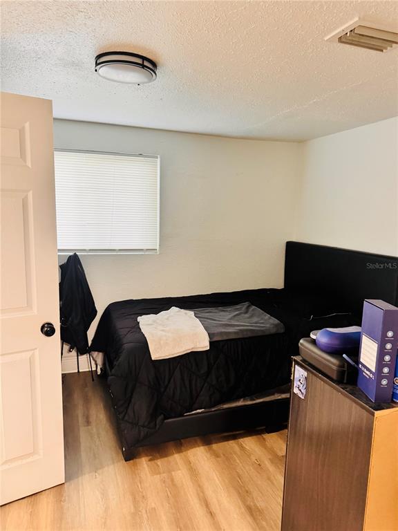 A bedroom features a black bed frame, light wood-look flooring, and a white window blind — 8710 N TANGERINE PLACE, TAMPA, FL