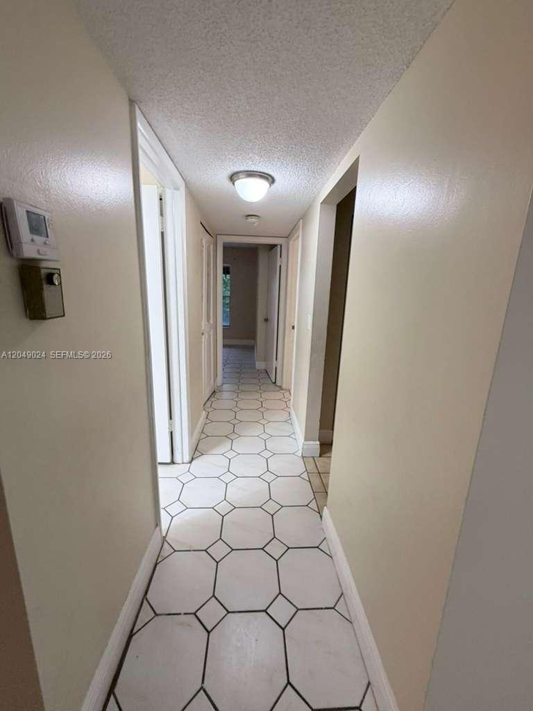 A narrow hallway features light-colored walls, a white ceiling, and white tile flooring with a geometric pattern — 3720 Inverrary Dr # 3L, Lauderhill FL 33319, LAUDERHILL, FL