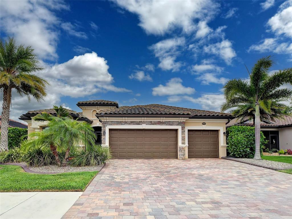 A single-story house with a three-car garage, stone accents, and palm trees under a blue sky — 20745 GRANLAGO DRIVE, VENICE, FL