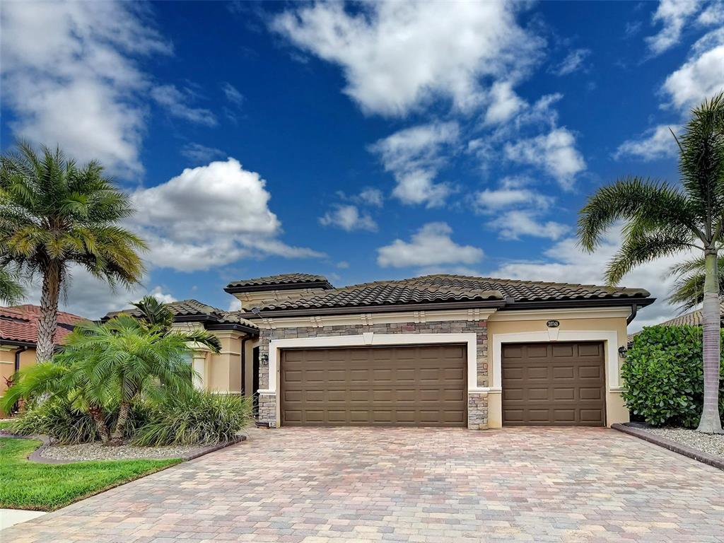 A single-story house with a three-car garage and a paved driveway under a blue sky — 20745 GRANLAGO DRIVE, VENICE, FL