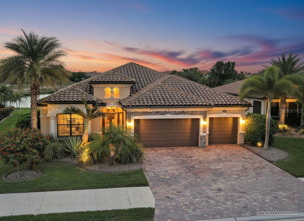 A single-story house with a tile roof, stone accents, and a paver driveway at dusk — 20745 GRANLAGO DRIVE, VENICE, FL