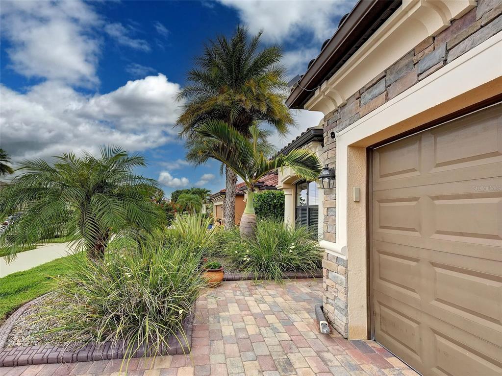 A paved walkway leads to a garage with stone accents and palm trees in front — 20745 GRANLAGO DRIVE, VENICE, FL