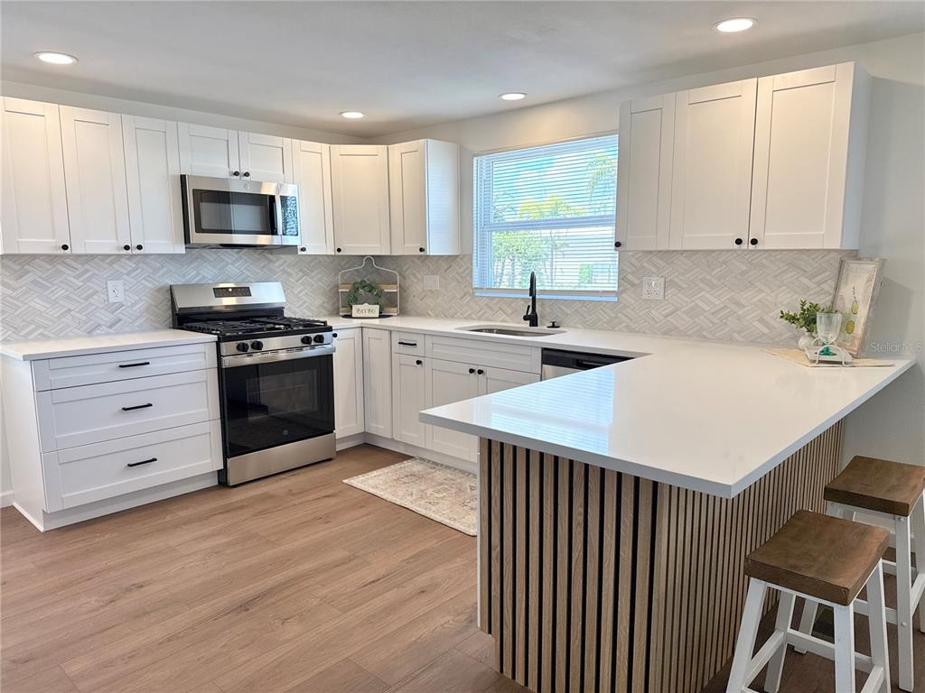 A modern kitchen features white shaker cabinets, stainless steel appliances, and a wood-slatted breakfast bar — 7271 MOUNT ARLINGTON DRIVE NE UNIT 430, ST PETERSBURG, FL