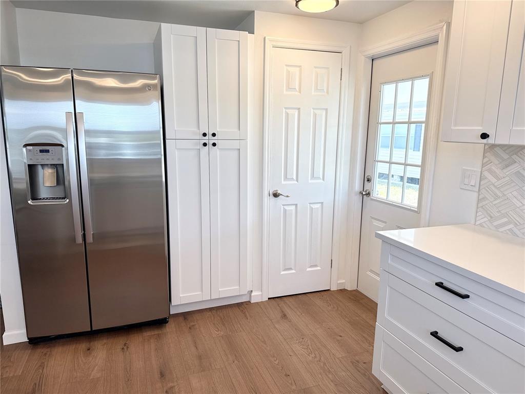 A kitchen features white cabinets, a stainless steel refrigerator, a pantry door, and wood flooring — 7271 MOUNT ARLINGTON DRIVE NE UNIT 430, ST PETERSBURG, FL