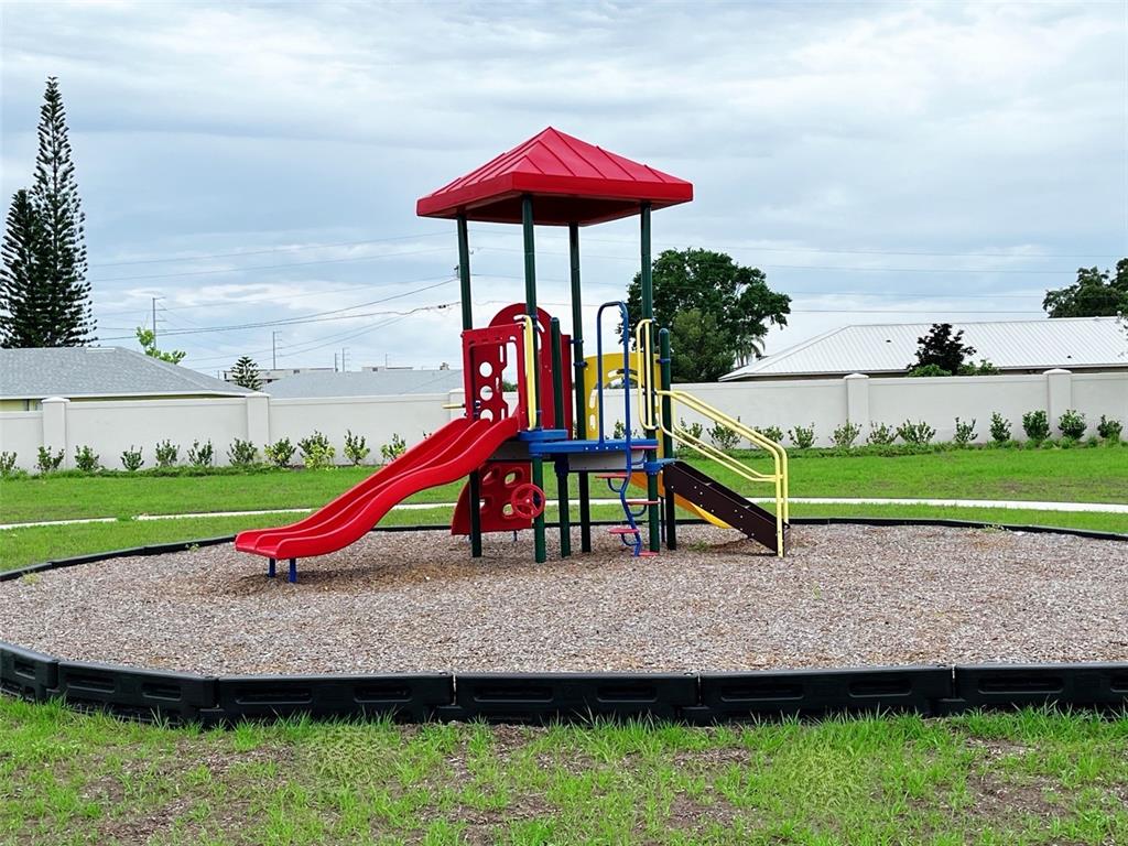 A colorful playground structure with a red roof sits in a wood-chipped area — 702 GINGER DRIVE, HAINES CITY, FL