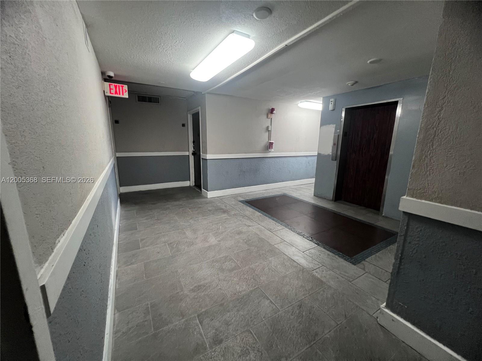 An indoor hallway features gray walls with white trim, tile flooring, and an elevator door — 496 NW 165th St Rd # 414, Miami FL 33169, MIAMI, FL