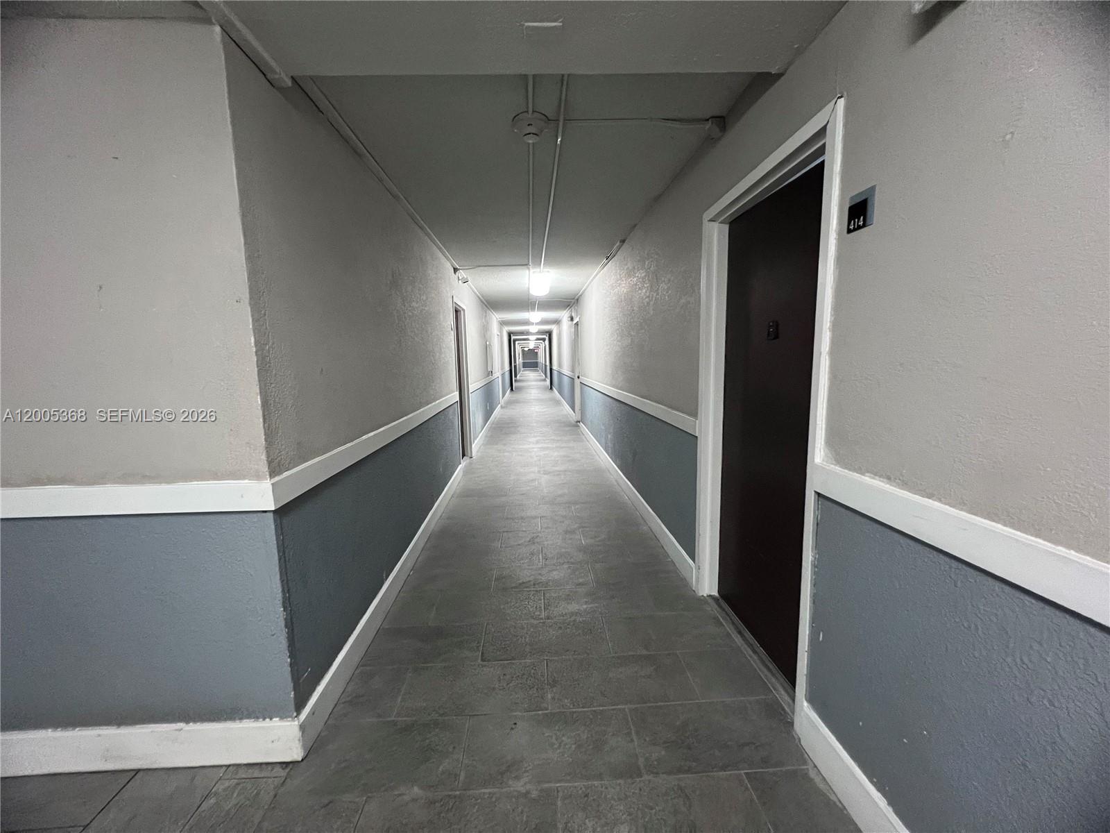 A long, narrow apartment hallway features gray walls with white trim and tiled flooring — 496 NW 165th St Rd # 414, Miami FL 33169, MIAMI, FL