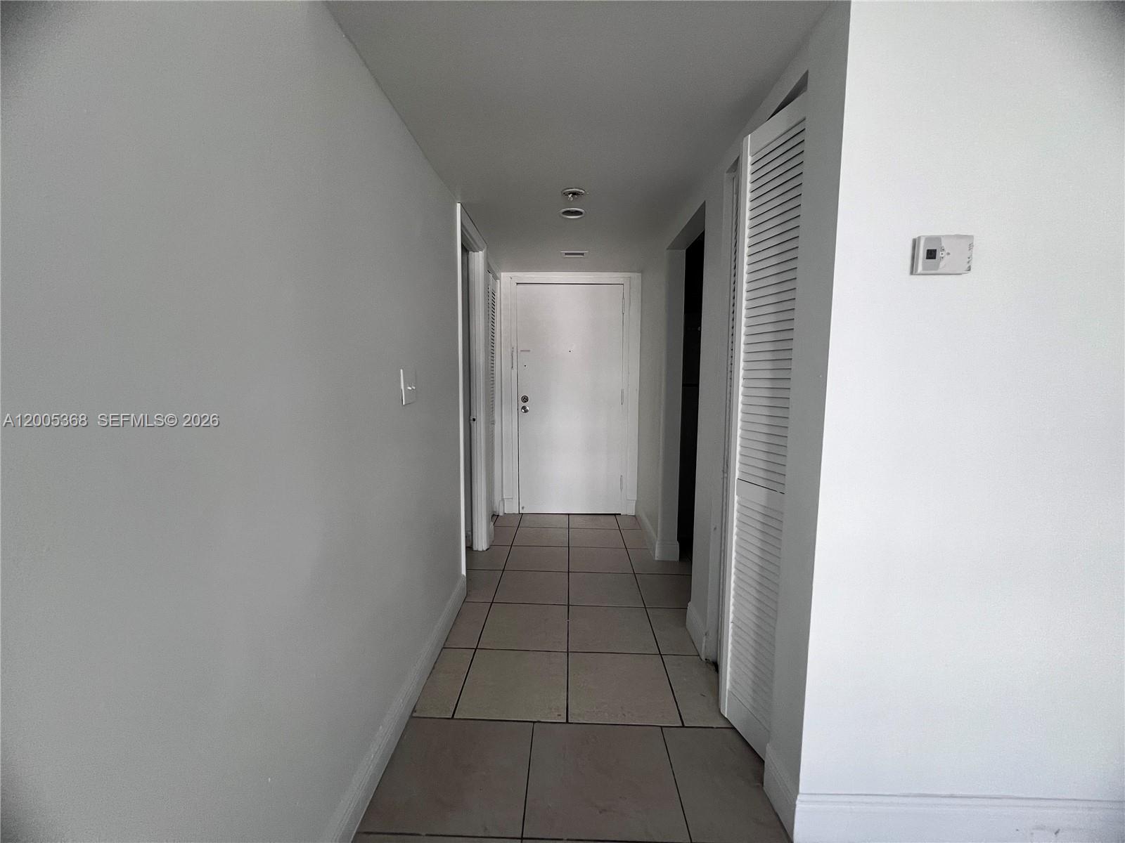 A hallway with white walls, tiled flooring, and a white door at the end — 496 NW 165th St Rd # 414, Miami FL 33169, MIAMI, FL