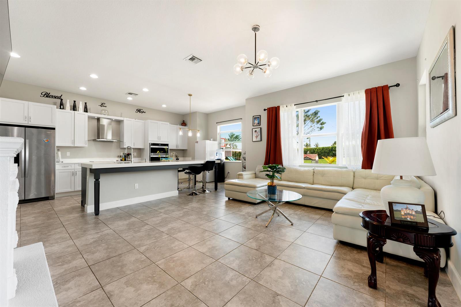 An open-concept kitchen and living area features white cabinetry, a large island, and white sectional — 5446 Macoon Way, Westlake FL 33470, WESTLAKE, FL