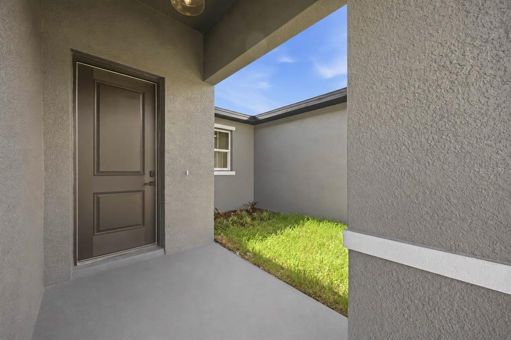 A covered entryway with a dark brown door leads to a small patch of grass — 2121 RIVER HAWK LOOP, WINTER HAVEN, FL