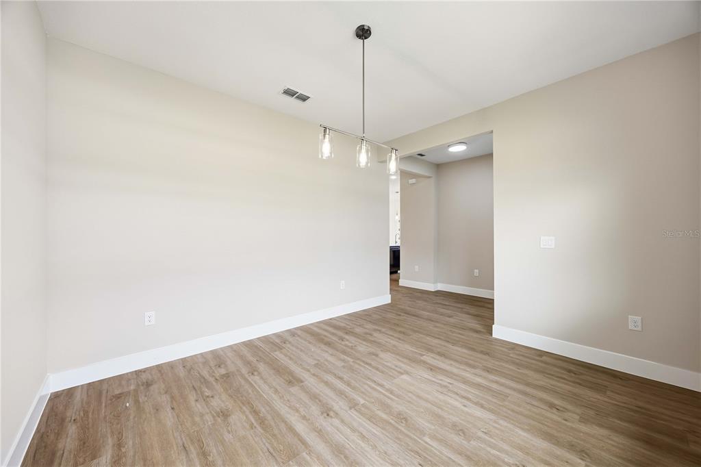 An empty dining room features light-colored walls, wood-look flooring, and a modern pendant light fixture — 2121 RIVER HAWK LOOP, WINTER HAVEN, FL