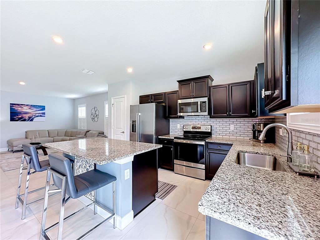 A kitchen features dark cabinetry, granite countertops, stainless steel appliances, and a central island — 3628 SAPPHIRE HOLLOW WAY, FORT PIERCE, FL