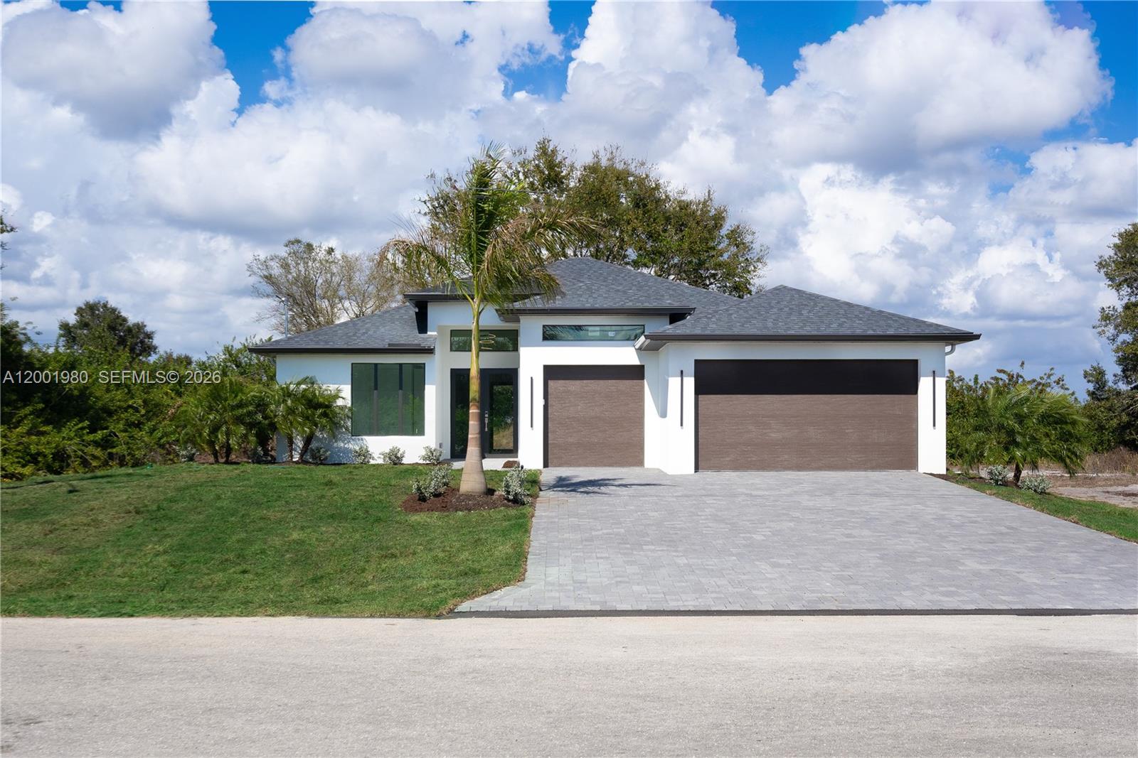A modern single-story house features a white exterior, dark garage doors, and a paved driveway — 529 N Theodore Vail, Lehigh Acres FL 33974, LEHIGH ACRES, FL