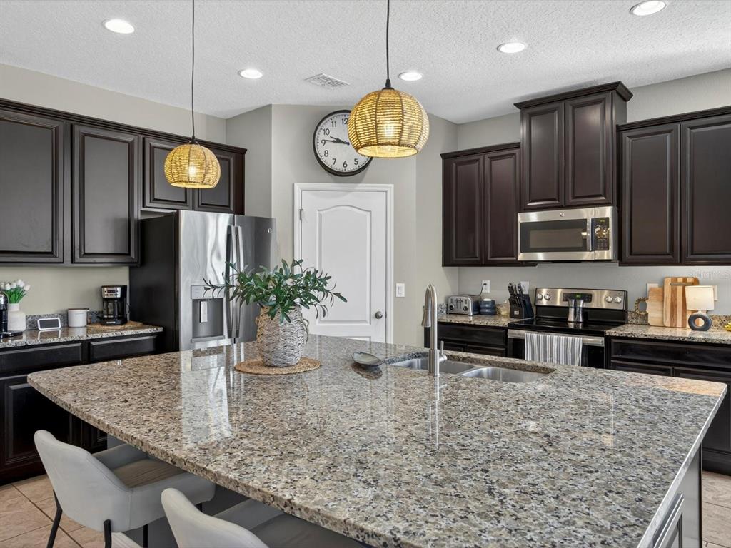 A kitchen features dark wood cabinets, granite countertops, a large island, and two pendant lights — 120 WHIRLAWAY DRIVE, DAVENPORT, FL