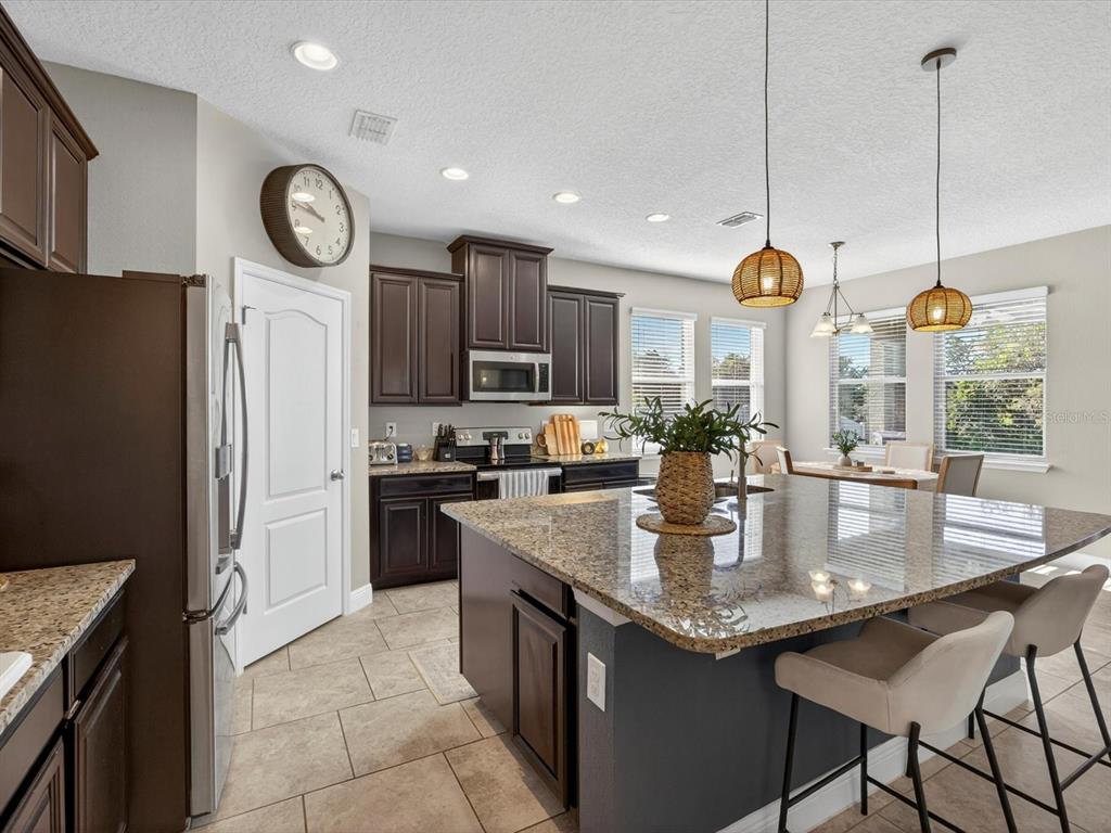 A kitchen features dark wood cabinets, granite countertops, a central island, and stainless steel appliances — 120 WHIRLAWAY DRIVE, DAVENPORT, FL
