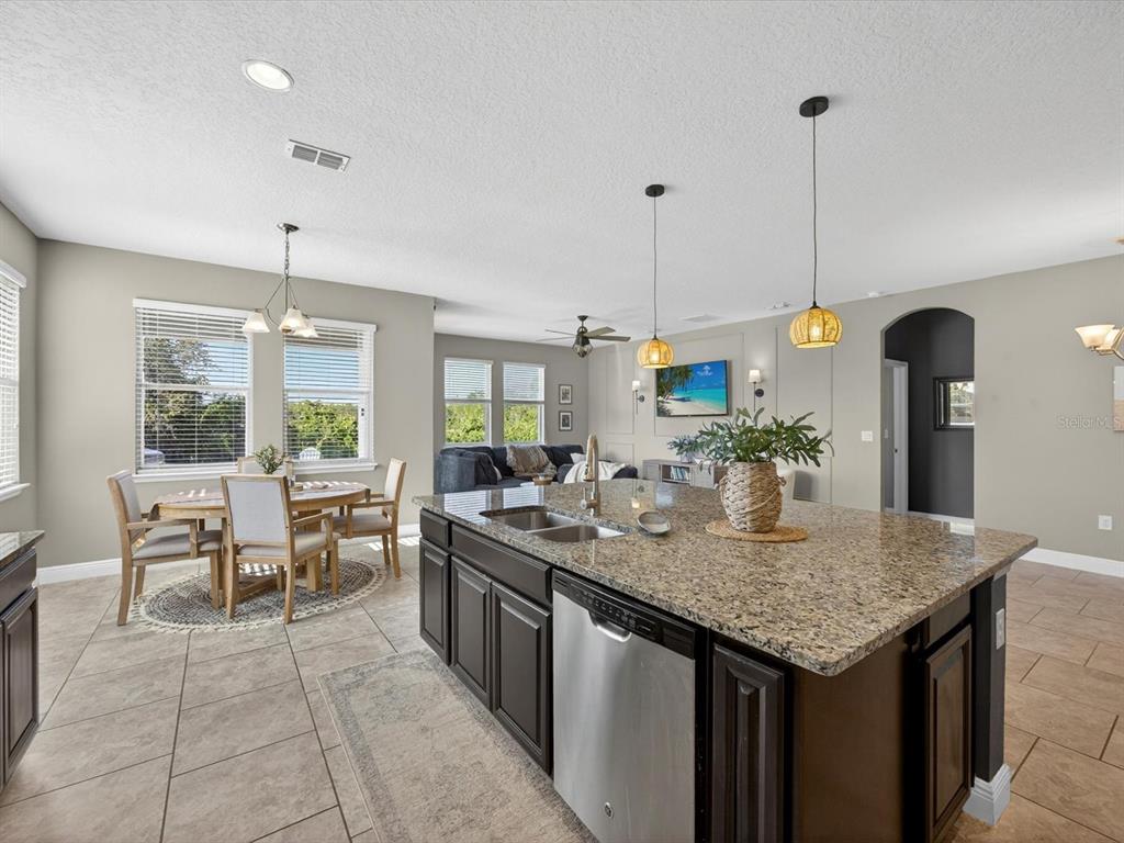 A kitchen with a granite island and dark cabinets overlooks a dining area and living room — 120 WHIRLAWAY DRIVE, DAVENPORT, FL