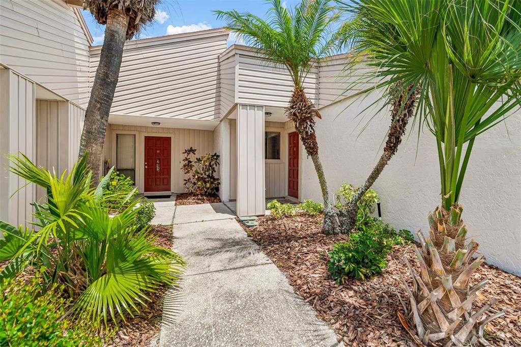 A concrete walkway leads to two red front doors of a tan-sided residential building — 4243 OAK LOOP UNIT 35, MULBERRY, FL