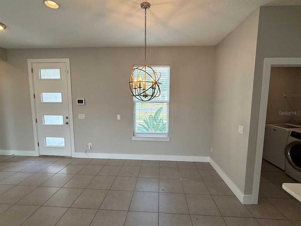 A dining area features a globe chandelier, tile flooring, a front door, and a window — 105 ZINNIA LANE W, KISSIMMEE, FL