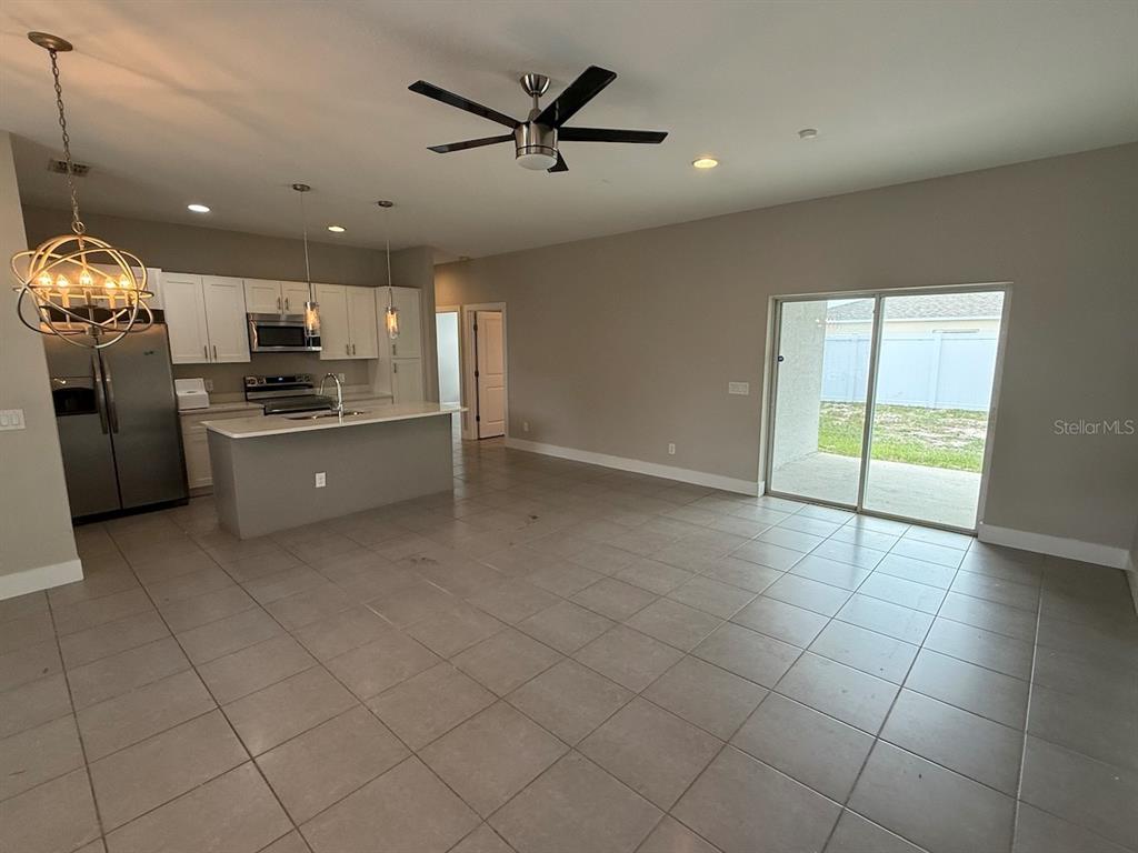An open-concept kitchen and living area with tile flooring, a center island, and sliding doors — 105 ZINNIA LANE W, KISSIMMEE, FL
