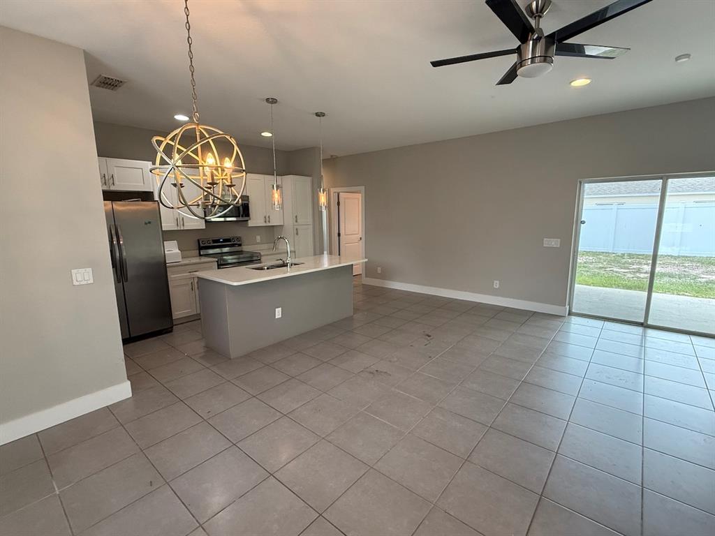 A kitchen with a center island, stainless steel appliances, and tile flooring opens to a patio — 105 ZINNIA LANE W, KISSIMMEE, FL