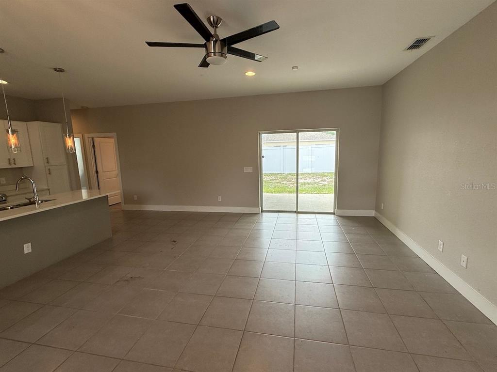 An open-concept living area features tile flooring, a ceiling fan, and sliding glass patio doors — 105 ZINNIA LANE W, KISSIMMEE, FL