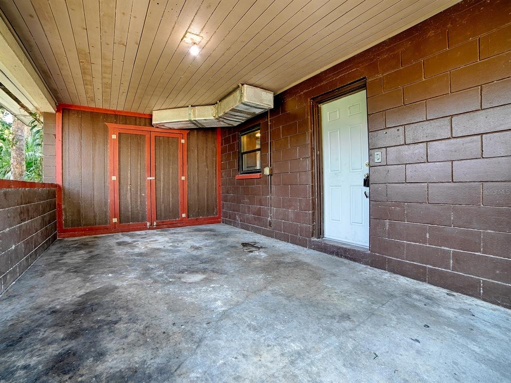 A covered concrete patio features brown block walls, wood paneling, and an exposed HVAC duct — 404 LOUIS STREET, LEESBURG, FL