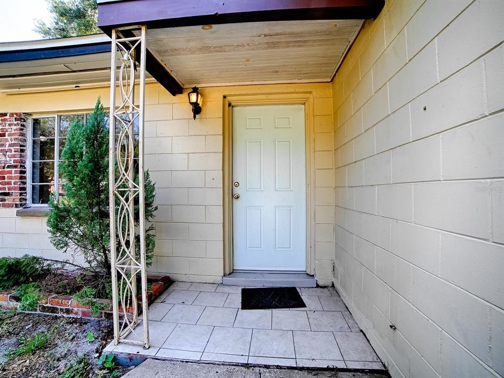 A white front door is centered on a porch with tiled flooring and a decorative column — 404 LOUIS STREET, LEESBURG, FL