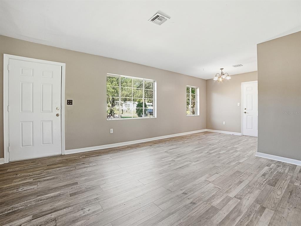 An empty room features light wood-look flooring, beige walls, two windows, and two white doors — 404 LOUIS STREET, LEESBURG, FL