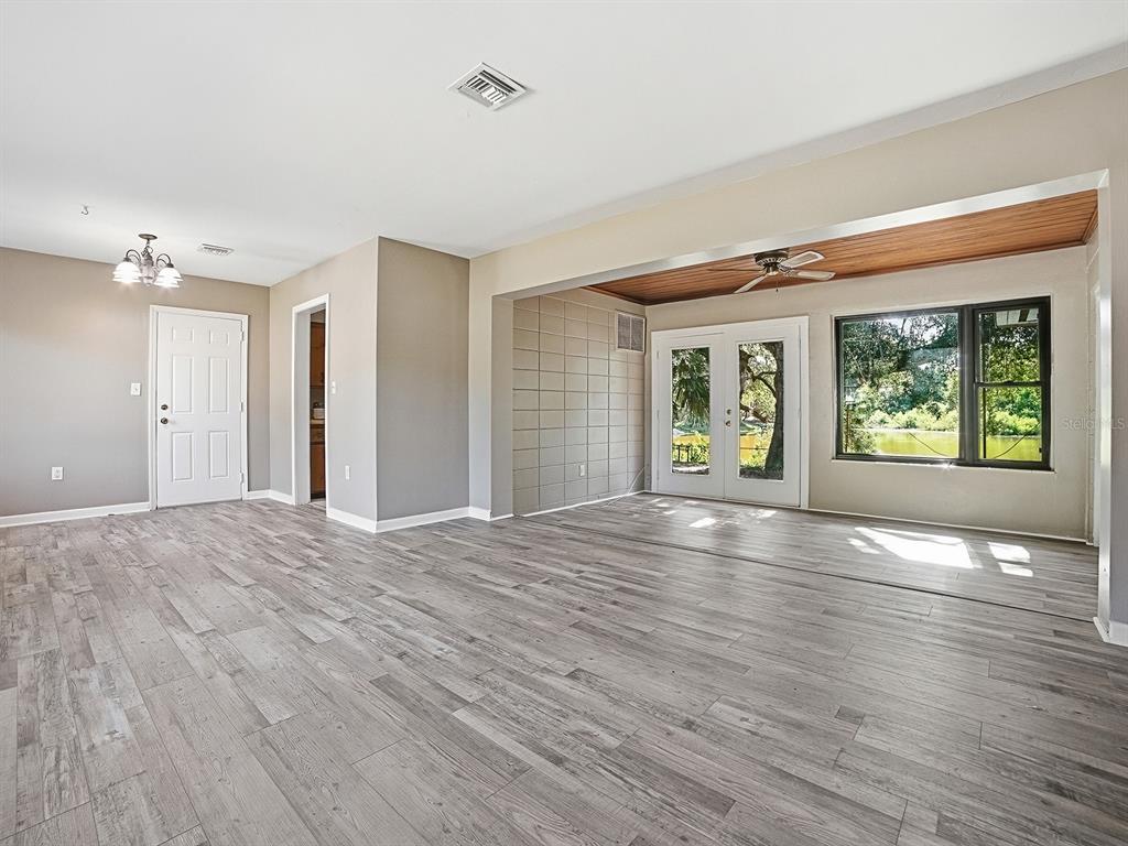 A living room with gray wood-look flooring, a wood-paneled ceiling, and glass doors to outside — 404 LOUIS STREET, LEESBURG, FL