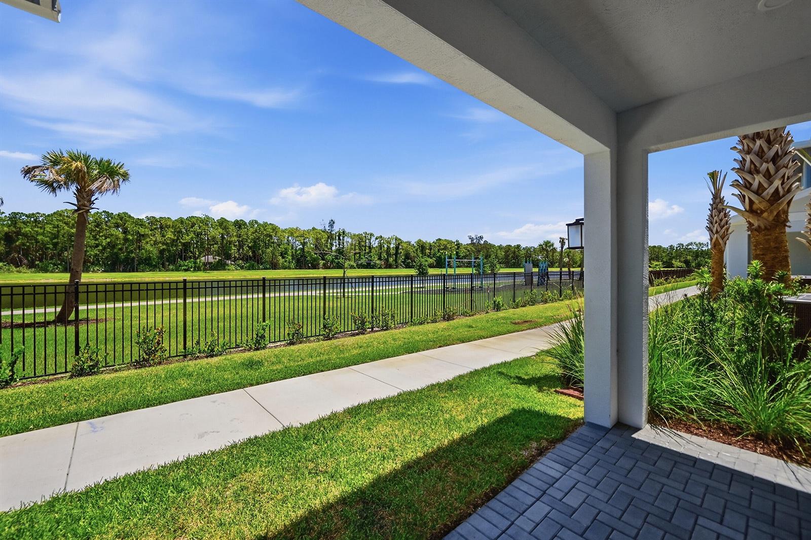 A covered patio overlooks a grassy yard, a metal fence, a pond, and a treeline — 4332 Brookgreen Square, Westlake FL 33470, WESTLAKE, FL