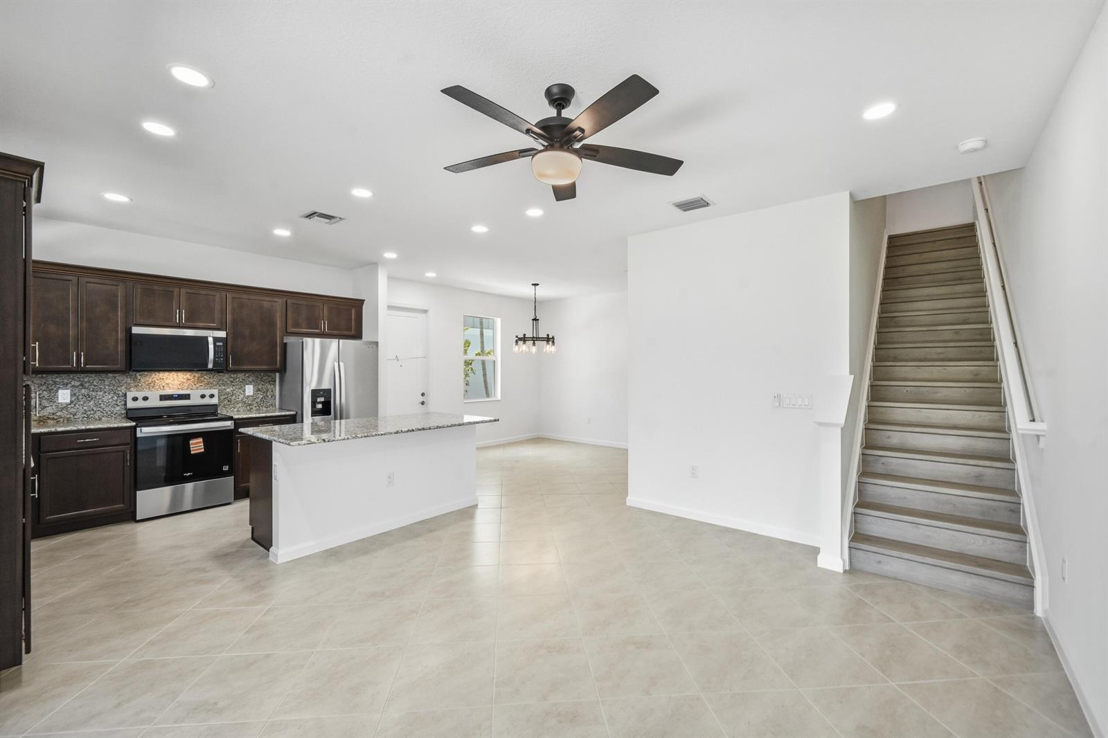 A kitchen with dark wood cabinets and granite countertops opens to a dining area and staircase — 4332 Brookgreen Square, Westlake FL 33470, WESTLAKE, FL