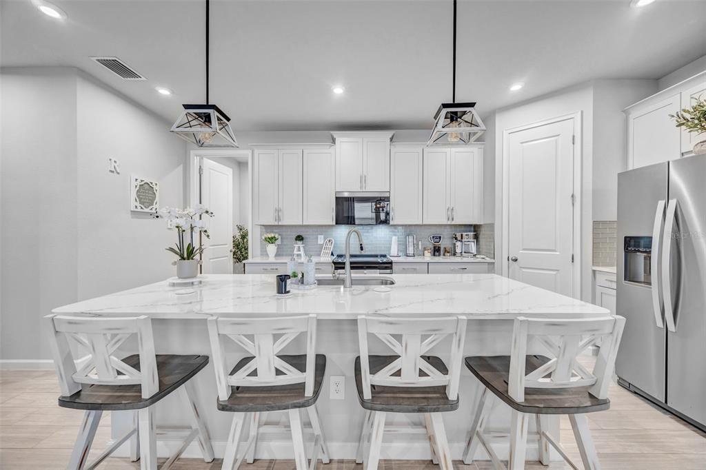 A modern kitchen features white cabinetry, a large marble-topped island, and four wooden bar stools — 5886 TIMBERDALE AVENUE, WESLEY CHAPEL, FL