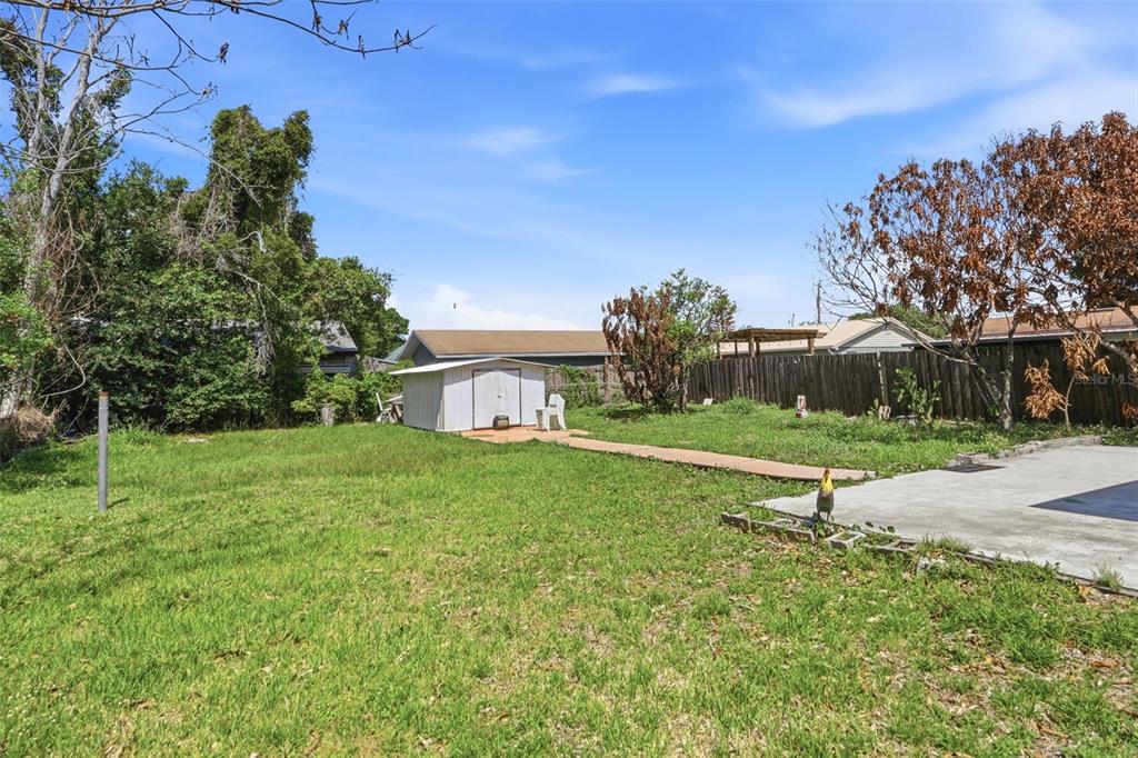 A grassy backyard features a small storage shed, a concrete patio, and a wooden fence — 6 VIOLA STREET, KISSIMMEE, FL