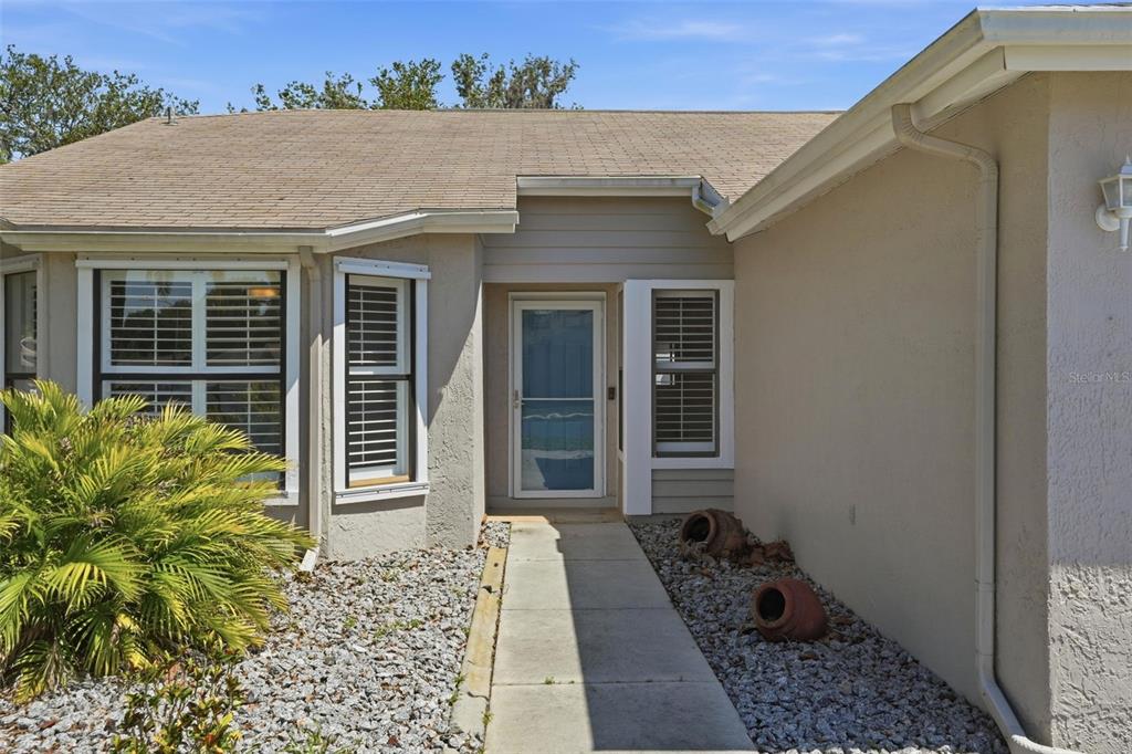The exterior of a beige house features a concrete walkway leading to the front door — 10616 BUCKS RUN, NEW PORT RICHEY, FL