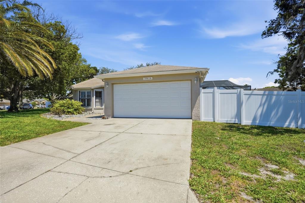 A beige single-story house features a two-car garage, a concrete driveway, and a white fence — 10616 BUCKS RUN, NEW PORT RICHEY, FL