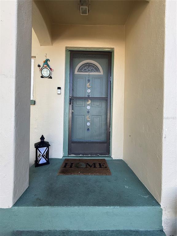 A teal front door with a screen door and a welcome mat sits on a porch — 6100 MAIN STREET UNIT A, NEW PORT RICHEY, FL