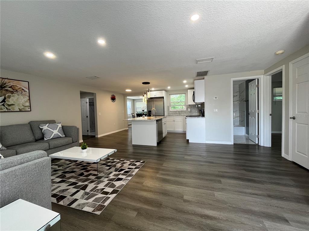 An open-concept living room and kitchen feature gray wood-look flooring and white cabinetry — 4457 TERRY LOOP, NEW PORT RICHEY, FL