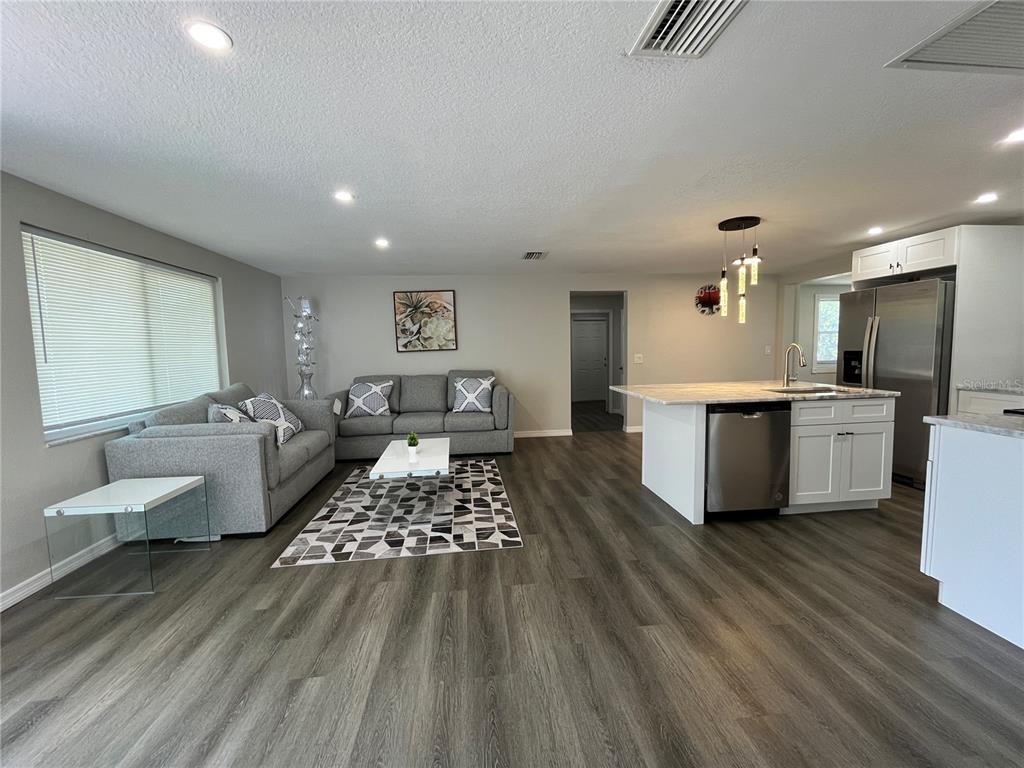 An open-concept living room features gray flooring, a sectional sofa, and a kitchen island — 4457 TERRY LOOP, NEW PORT RICHEY, FL