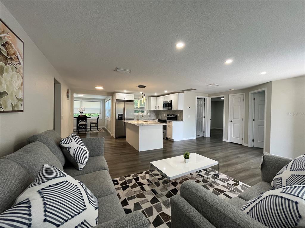 An open-concept living room and kitchen featuring gray flooring, white cabinetry, and a center island — 4457 TERRY LOOP, NEW PORT RICHEY, FL
