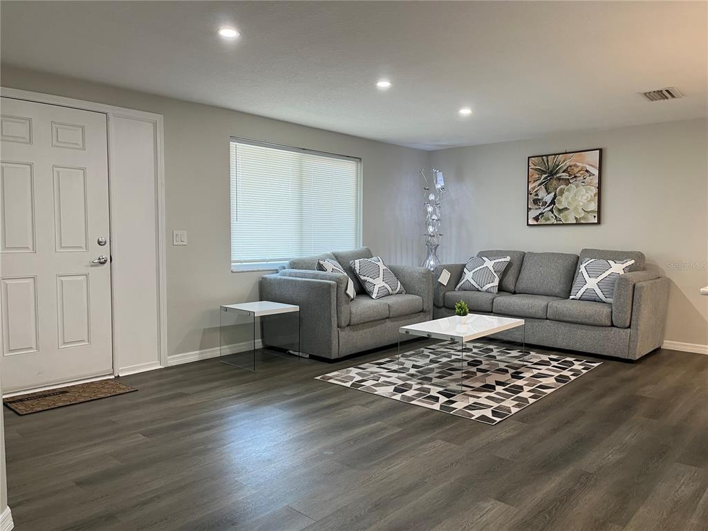 A living room features gray sofas, a geometric rug, and wood-look flooring — 4457 TERRY LOOP, NEW PORT RICHEY, FL